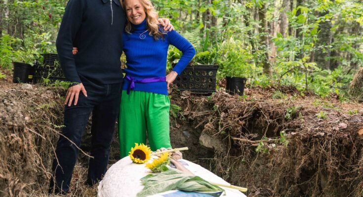 Een man en een vrouw staan naast hun armen in elkaar in bossen. Ze staan in een greppel naast een doodskist van champignons met zonnebloemen hierboven geplaatst.